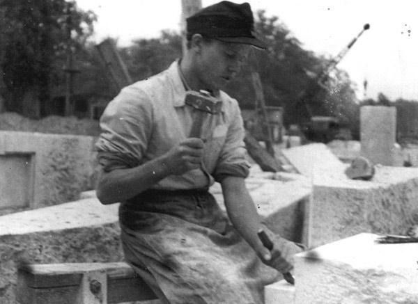 Ein Mann mit Hut und Latzhose bearbeitet einen Stein